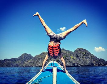 Man doing handstand on boat in sea against blue sky