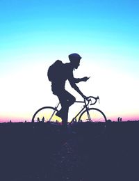 Silhouette person riding bicycle against sky during sunset