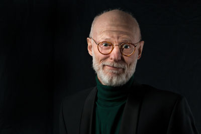 Portrait of smiling senior man wearing eyeglasses against black background