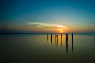 Wooden posts in sea against sky during sunset