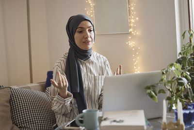 Young businesswoman wearing hijab and discussing on video call over laptop at home