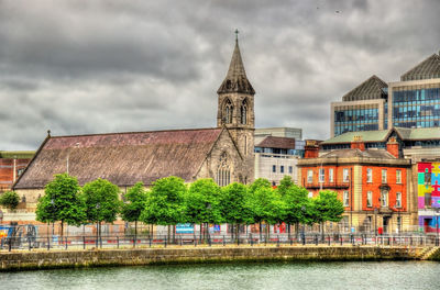 Buildings by river against cloudy sky