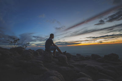 Man sitting on rock at beach during sunset