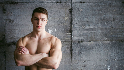 Close-up portrait of shirtless muscular man standing by wall