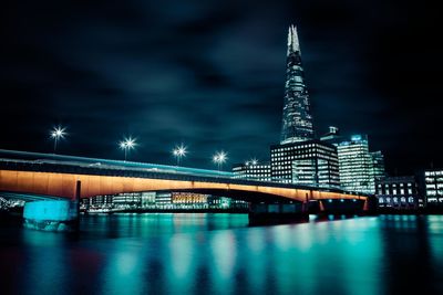 Bridge over thames river with reflection against modern buildings at night