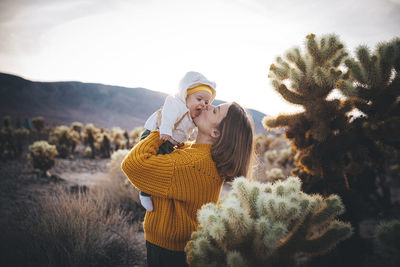 A woman with a baby is standing near a cactus in the desert