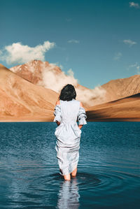Rear view of woman standing in lake against mountain and sky