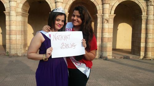 Portrait of smiling females showing placard while standing against building