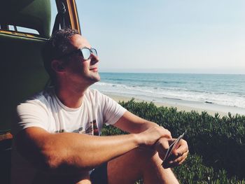 Young man using mobile phone while sitting on beach