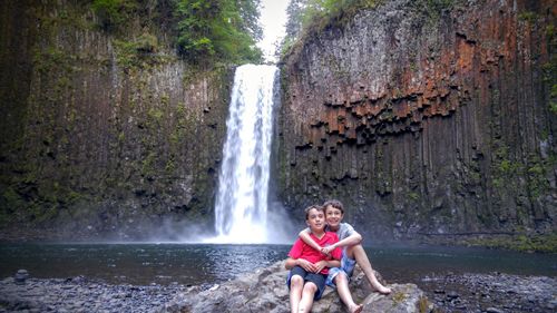 Portrait of brothers sitting on rock against waterfall