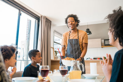 Cheerful man serving food to family at dining table