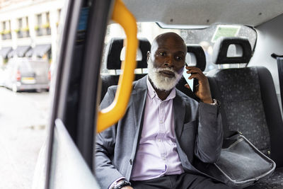 Senior bearded passenger talking on mobile phone in taxi