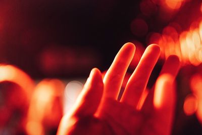 Close-up of human hand against illuminated defocused lights at night