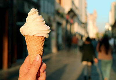 Closeup vanilla soft serve ice cream cone in hand with blurry walking street in backdrop