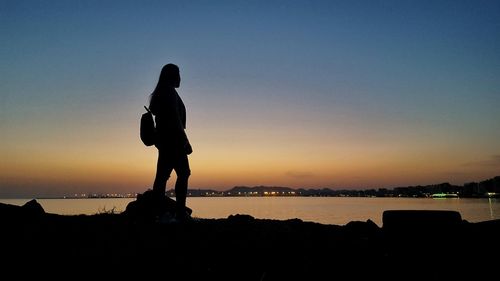 Silhouette man standing by sea against sky during sunset