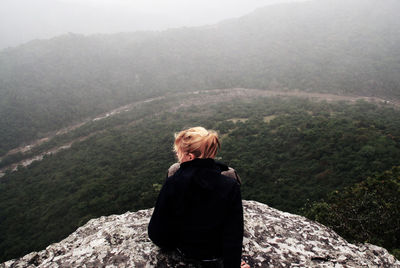 High angle view of woman sitting on cliff against mountains