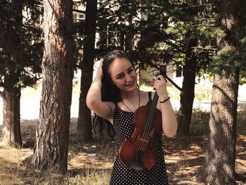 Portrait of beautiful woman holding violin against trees