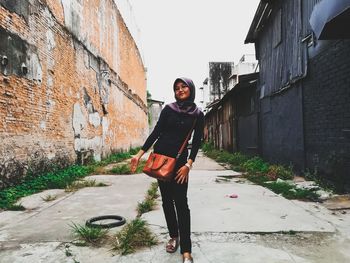 Full length portrait of young woman standing against sky