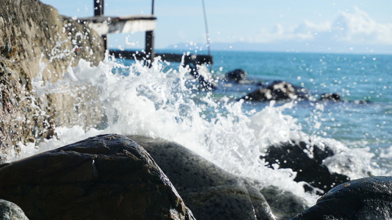 PANORAMIC VIEW OF WAVES SPLASHING ON ROCKS AGAINST SEA