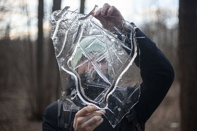 Man holding ice while standing outdoors during winter