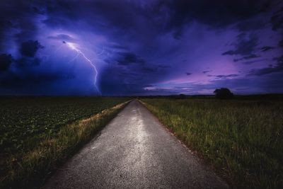 Empty road amidst fields during stormy night