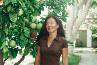 Portrait of young woman standing against orange tree