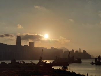 Silhouette buildings by sea against sky during sunset