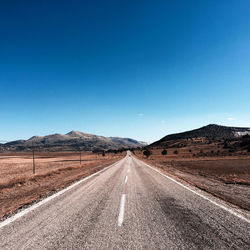 Road leading towards mountains against clear blue sky