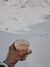 Close-up of hand holding coffee cup against sky