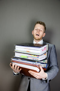 Tired businessman holding stacked files against gray background