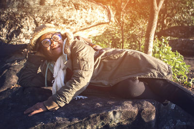 Portrait of smiling senior woman lying on rock at forest