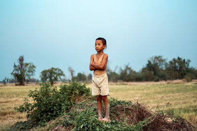 Thoughtful boy with arms crossed standing on field against sky at farm