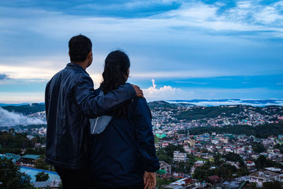 Young couple watching downtown city view with dramatic cloudy sky at evening from mountain top