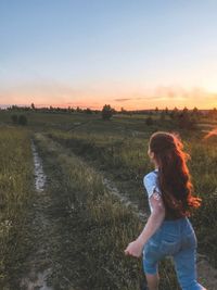 Woman standing on field against sky during sunset