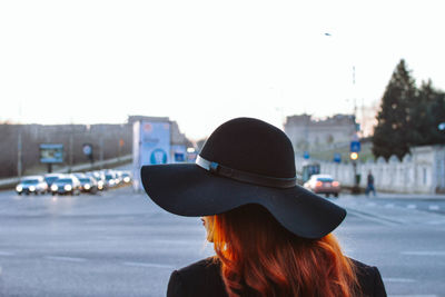 Rear view of woman wearing hat standing on road against sky in city