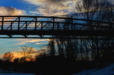 Silhouette bridge over river against sky at sunset