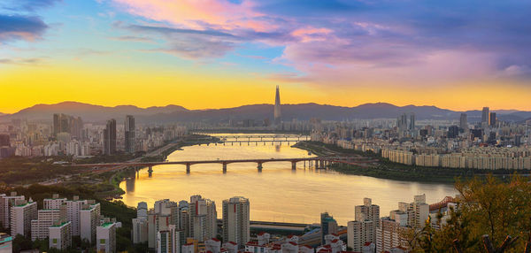 Bridge over river in city against sky during sunset