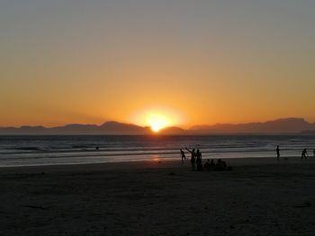 Silhouette people on beach against sky during sunset