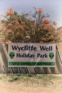 Information sign by trees on field against sky