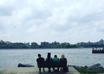 Rear view of people sitting on riverbank against sky