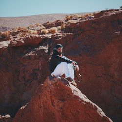 Portrait of man sitting on rock formation during sunny day