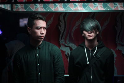 Close-up of male friends standing against wall at night