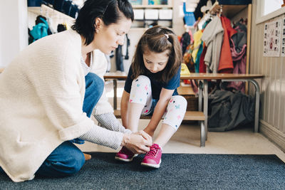 Side view of teacher helping girl wearing shoes in cloakroom at preschool