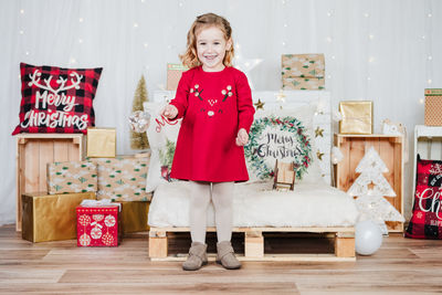 Cute blonde little girl wearing red christmas dress at home over christmas decoration. holiday