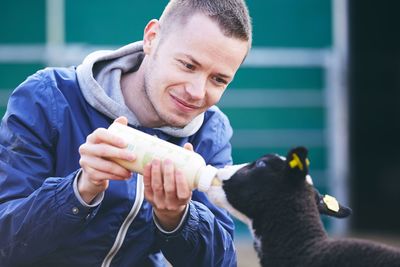 Smiling mid adult man feeding milk to lamb