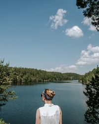 Rear view of young woman looking at lake while sitting against sky