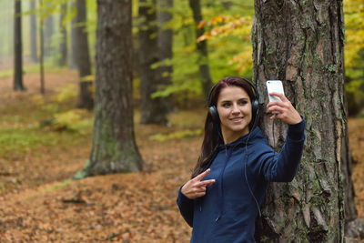 Young woman using phone while standing on tree trunk in forest
