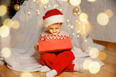 Happy kid sitting with gift by christmas decoration