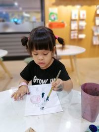 Girl painting on paper at table in classroom