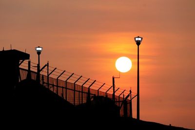 Silhouette street light by sea against orange sky